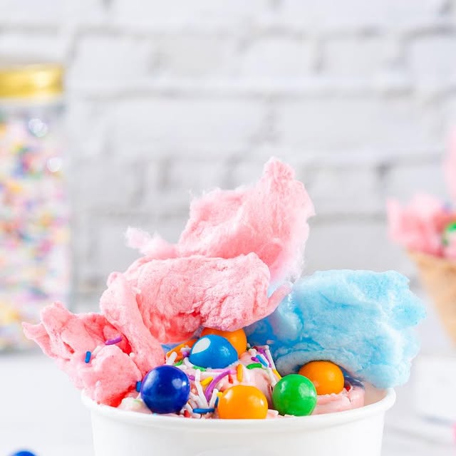 Cotton candy ice cream rolls topped with pink and blue cotton candy, gumballs, and sprinkles